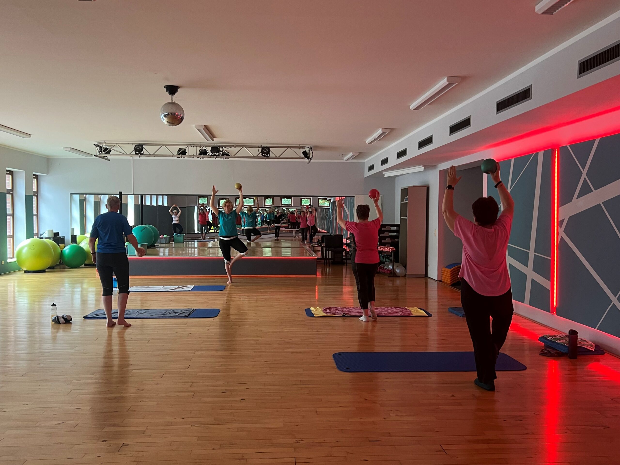 Gruppenkurs. Teilnehmer stehen in einer Yoga Position und halten in der Luft einen Ball