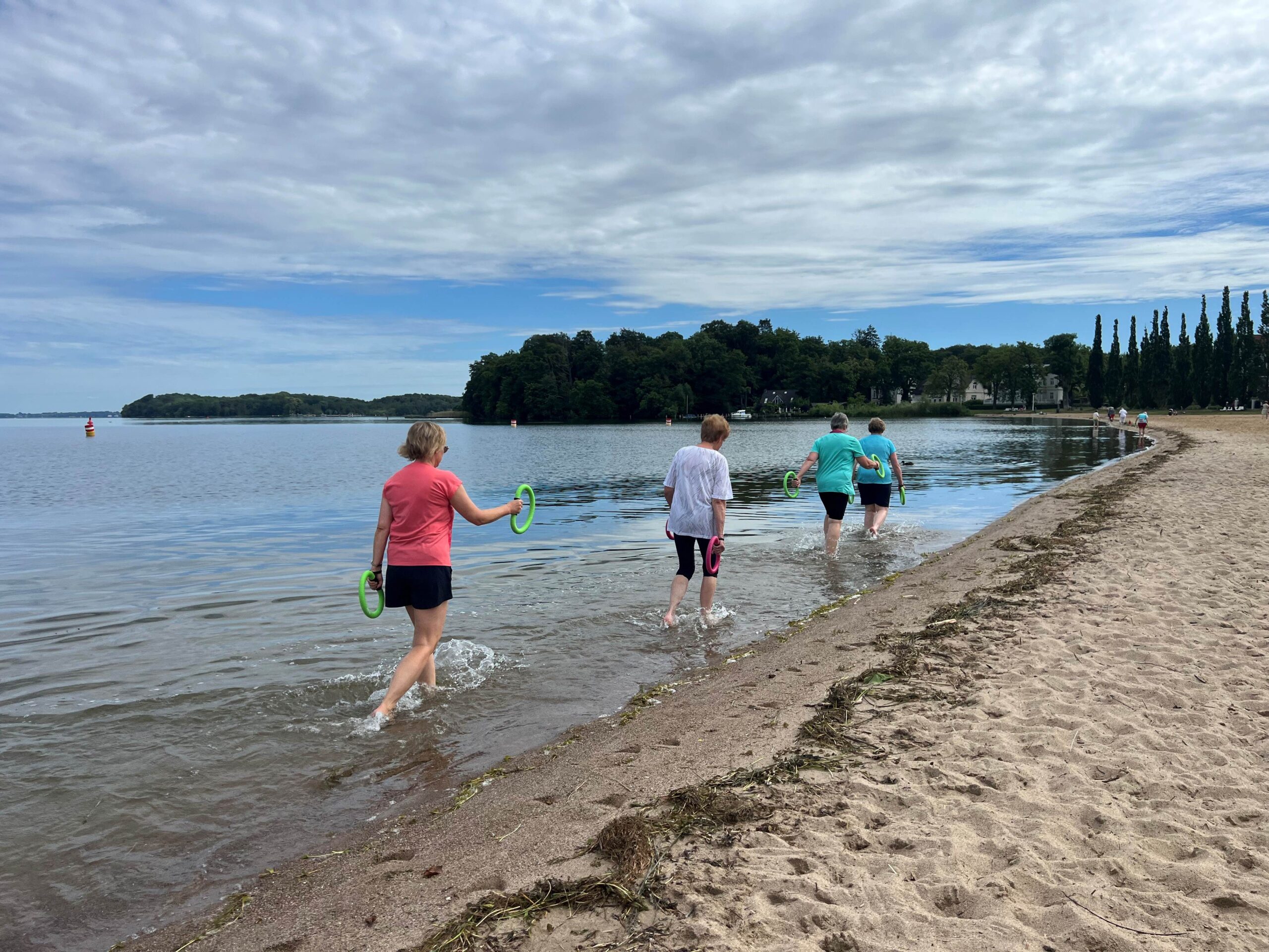 Gruppenkurs draußen am Zippendorfer Strand. Teilnehmer laufen im Wasser und schwingen mit Schwing-Ringen